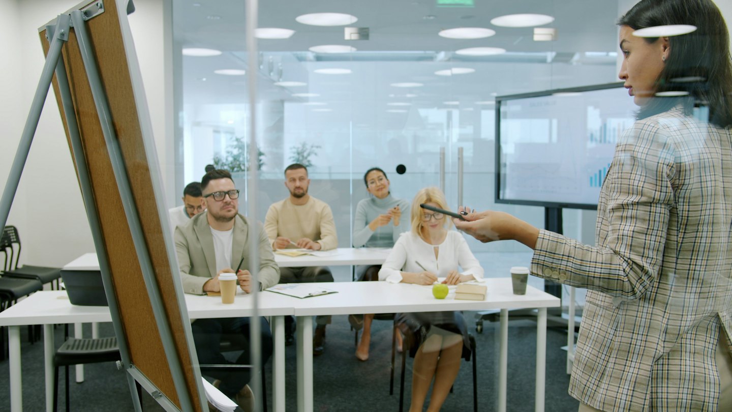 Woman presenting business charts to attentive colleagues in an office.